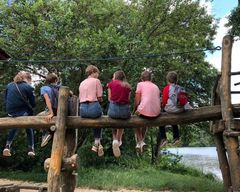 Jugendliche auf einem Baumstamm sitzend (mit dem Rücken zum Fotografen)